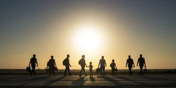 Grupo diverso de refugiados e migrantes caminhando em direção ao pôr do sol, simbolizando esperança no Brasil.