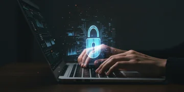 Mãos digitando em um teclado de notebook com um cadeado holográfico, simbolizando a segurança contra crimes cibernéticos e fraudes digitais.